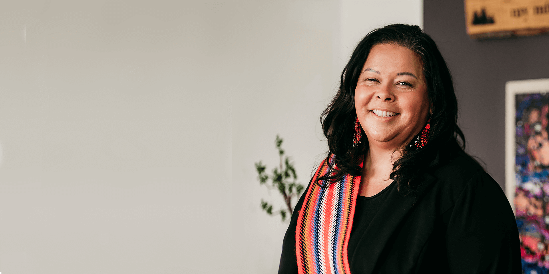 Angie Saltman standing in an office environment wearing a Metis sash over her right shoulder