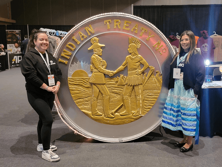 Natalya and Brandi standing next to large replica of Indigenous Treaty Coin