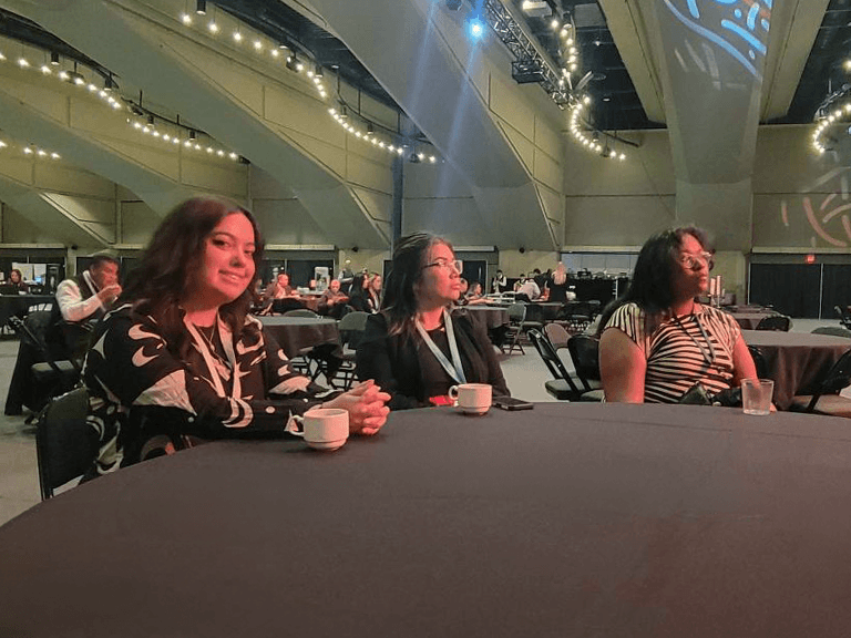 Natalya, Brandi, and Ellie seated at a table listening to a presentation at the Indigenous Trailblazers Summit.